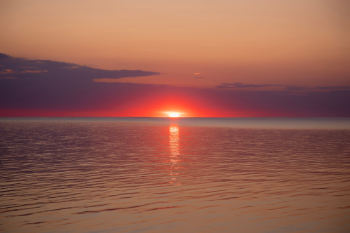 A serene sunset over calm waters, with vibrant orange and purple hues reflecting on the surface.