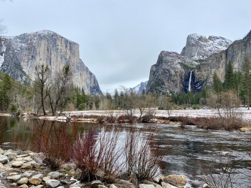 A serene view of Yosemite Valley, featuring towering cliffs, a river, and snow-dusted trees in a tranquil landscape.