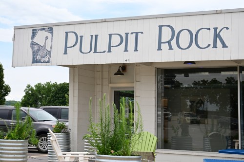 Sign for "Pulpit Rock" on a building exterior, with greenery and outdoor seating visible.