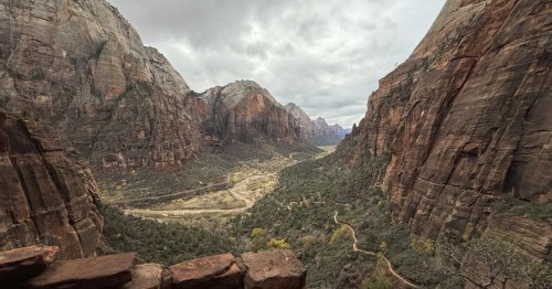 Standing at the top of an overlook, staring at a deep canyon, river, and trails, within Zion National Park.