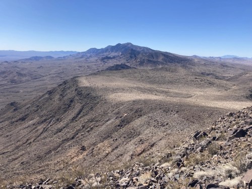 A vast, arid landscape with rocky terrain and distant mountains under a clear blue sky.