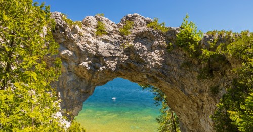 A limestone arch frames a white boat on the aquamarine water of Lake Huron under a blue sky.