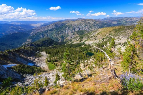 A panoramic view of a mountainous landscape with lush greenery, rocky terrain, and a clear blue sky.