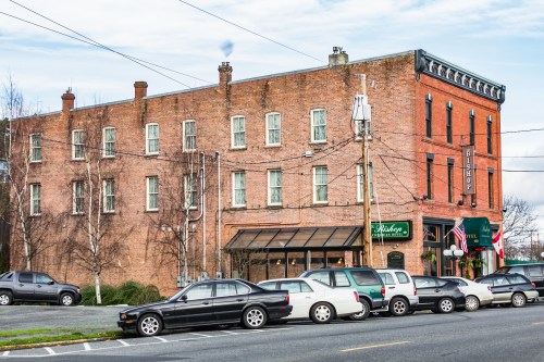 Historic brick building with multiple windows, featuring a restaurant and parked cars in front.