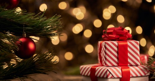 Two red and white striped presents sit next to a Christmas Tree with lights in the background.