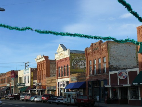 Historic downtown street with brick buildings, shops, and festive decorations under a clear blue sky.