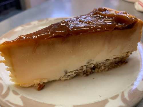 A slice of creamy caramel cheesecake on a plate, featuring a glossy caramel topping and a nutty crust.