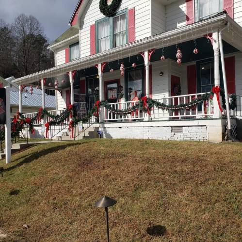 A festive house decorated with wreaths, garlands, and ornaments, with a person on the porch and a "Open" sign visible.
