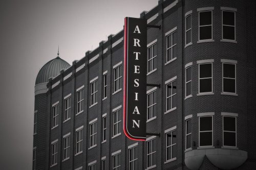 Sign for "Artesian" on a brick building, featuring a distinctive architectural design and a dome in the background.