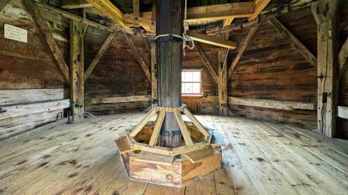 Interior of a wooden structure featuring a central support post and rustic wooden beams, with a warm, inviting atmosphere.