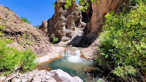 A serene river flows through a rocky canyon, surrounded by lush greenery and bright blue skies.