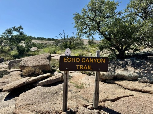 Sign for Echo Canyon Trail surrounded by rocky terrain and sparse vegetation under a clear blue sky.
