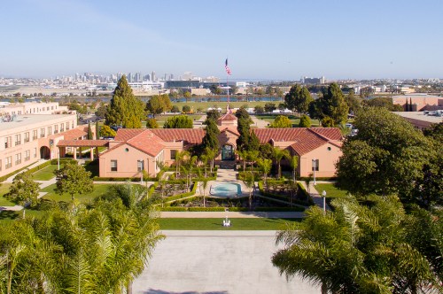Aerial view of a landscaped courtyard with buildings, palm trees, and a city skyline in the background.
