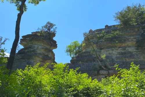 Two tall rock formations surrounded by lush green foliage under a clear blue sky.