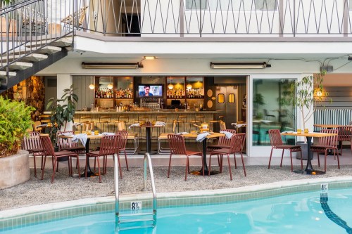 A poolside dining area with tables and chairs, featuring a bar and a TV in a modern setting.