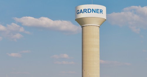 a water town sporting the town name of gardner on it in blue letters stands tall over the town with blue sky above