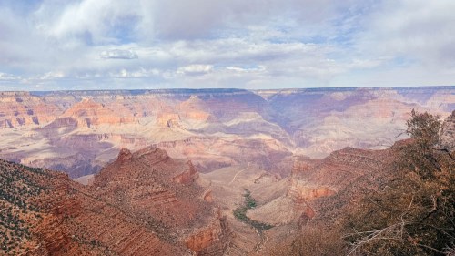 A panoramic view of the Grand Canyon, showcasing layered rock formations and a cloudy sky.