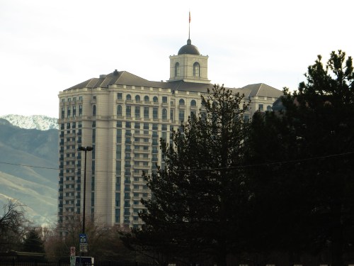 A tall hotel building with a dome and flag, surrounded by trees and mountains in the background.