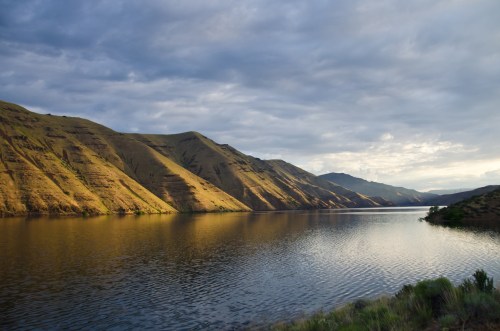 A serene lake surrounded by rolling hills under a cloudy sky, reflecting the landscape in calm waters.