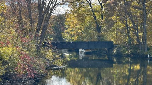 A serene scene of a bridge over a calm river, surrounded by vibrant autumn foliage.