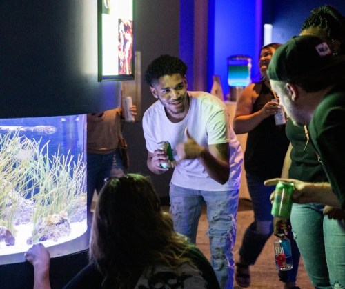 A group of people enjoying an aquarium exhibit, with one man giving a thumbs up while holding a drink.