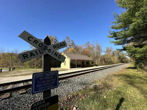 A railroad crossing sign beside railroad tracks and a historic depot in Cuyahoga Valley National Park.