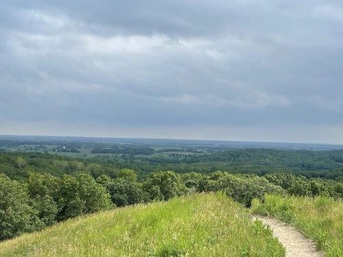 A scenic view of rolling green hills under a cloudy sky, with a winding path leading through the landscape.