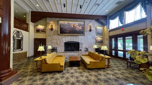Cozy hotel lobby with two yellow sofas, a stone fireplace, and artwork on the walls, featuring warm lighting and decor.