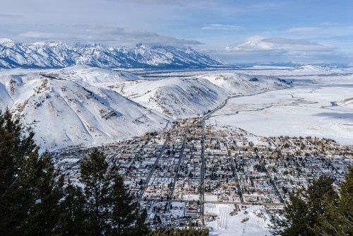 Aerial view of a snowy town surrounded by mountains and a frozen landscape under a clear blue sky.