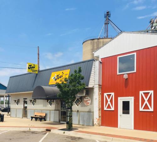 A small restaurant with a yellow sign, a gray roof, and a red barn-style building next door, set against a blue sky.