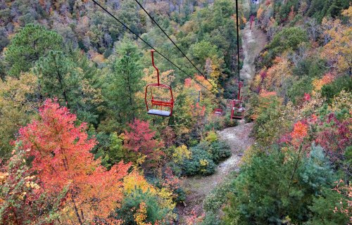 Aerial view of a ski lift surrounded by vibrant autumn foliage in shades of red, orange, and green.