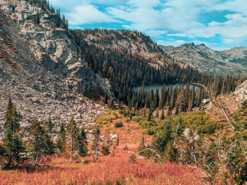 A scenic view of a mountainous landscape with a lake surrounded by evergreen trees and autumn foliage.