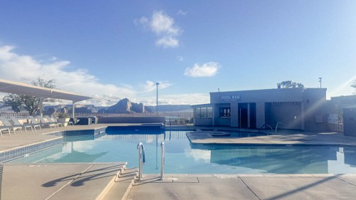 A serene pool area with a bar, lounge chairs, and mountains in the background under a clear blue sky.