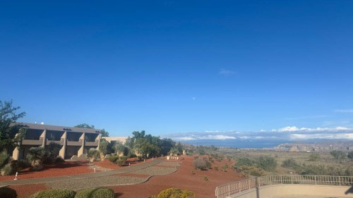 A clear blue sky over a landscaped area with shrubs and a distant view of hills and clouds.