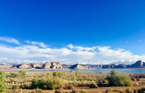 A scenic landscape featuring a blue sky, rocky formations, and a calm body of water surrounded by greenery.