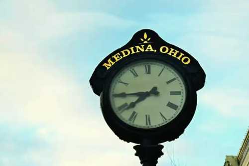 A historic clockface with "MEDINA, OHIO" written on it stands before a blue sky.