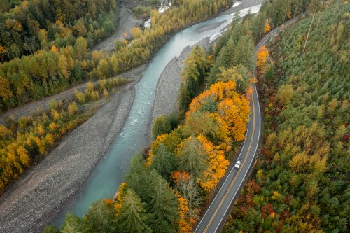 Aerial view of a winding river surrounded by autumn trees and a road, showcasing vibrant fall colors.