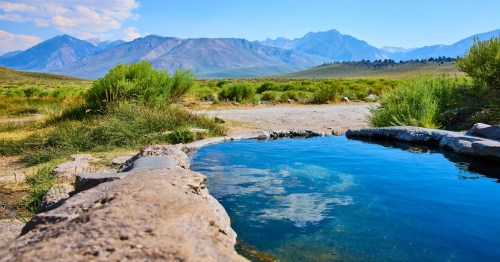 Crystal clear waters of The Rock Tub Hot Springs reflect the vast Sierra Nevada mountains and vibrant grasses near Mammoth Lakes California on a sunny day inviting relaxation and adventure.