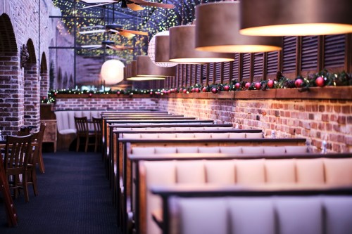 Cozy restaurant interior with brick walls, festive decorations, and illuminated pendant lights over booth seating.