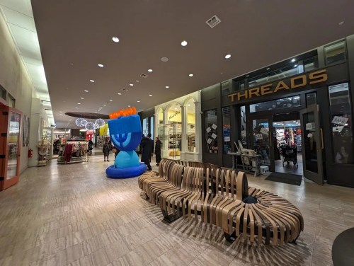 A spacious indoor shopping area featuring a large blue inflatable menorah and a modern wooden bench.
