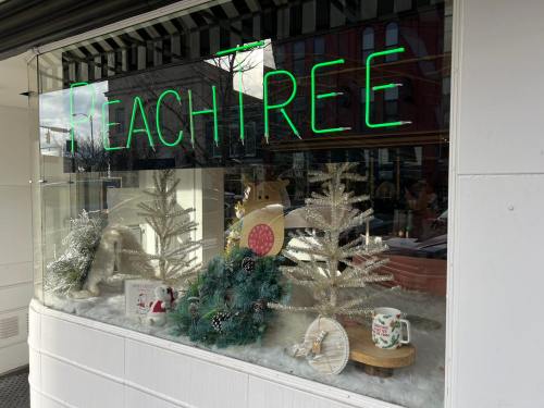 A festive window display featuring silver Christmas trees, decorations, and a neon "PeachTree" sign.