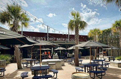 Outdoor seating area at Edmund's Oast Brewing Co., featuring palm trees and umbrellas on a sunny day.