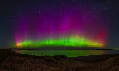 A vibrant aurora borealis displays shades of green and purple over a calm body of water, under a starry night sky.