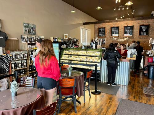 A cozy café interior with customers at the counter and a display case of pastries, featuring wooden floors and brick walls.