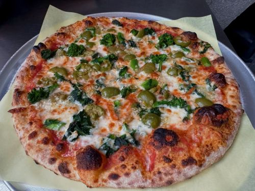 A freshly baked pizza topped with green peppers, olives, broccoli, and spinach on a golden crust.
