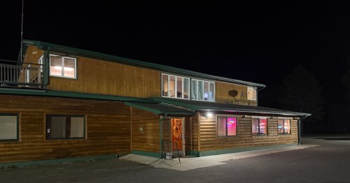 A wooden building at night with illuminated windows and a sign, set against a dark sky.