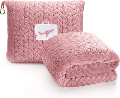A soft pink blanket folded next to a matching carrying pouch with a travel-themed design.
