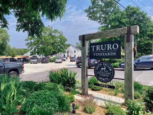 Sign for Truro Vineyards with a parking area and greenery in the background on a sunny day.