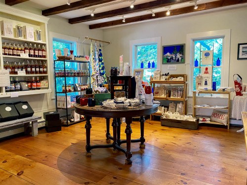 A cozy shop interior featuring wooden floors, shelves of products, and a central table with various items for sale.