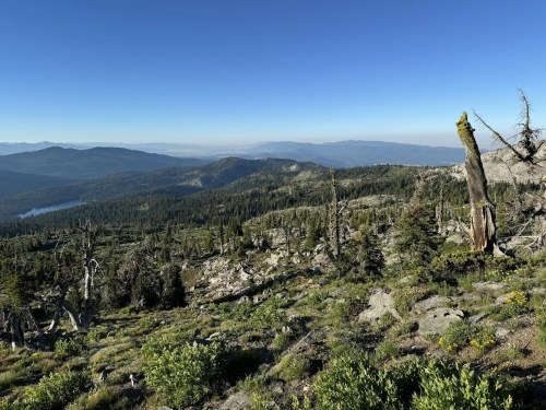 A panoramic view of a mountainous landscape with green trees, rocky terrain, and a clear blue sky.